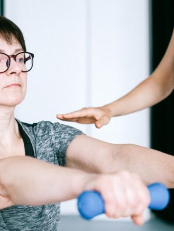 A personal trainer guides a woman in exercising with dumbbells for fitness and strength training.