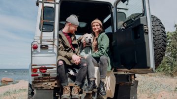 Young couple relaxing by the ocean in a van with their dog on a sunny day.