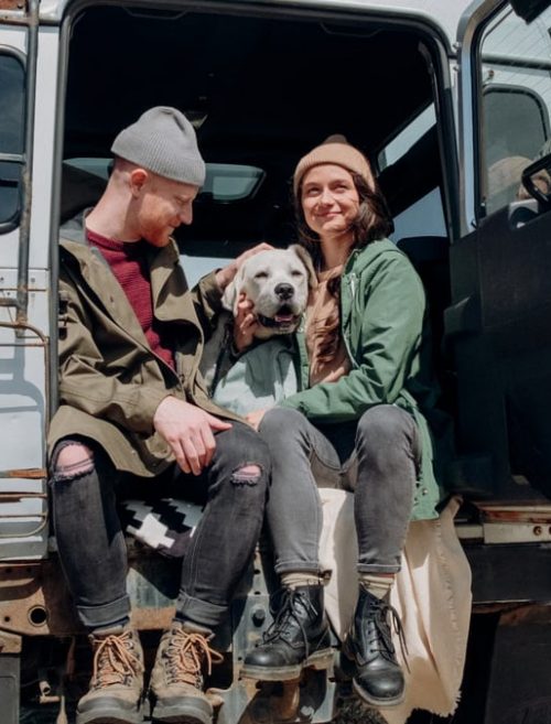 Young couple relaxing by the ocean in a van with their dog on a sunny day.